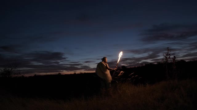 野蛮人用火炬探索乡村。低角度的人与弓和燃烧的火炬探索荒野在夜晚对多云的天空视频素材