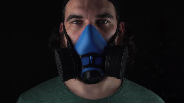 在黑暗的背景下，一个戴着蓝色呼吸器的男人的近距离镜头。视频下载