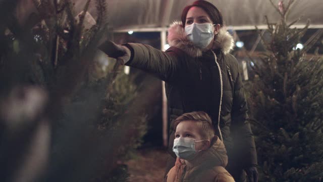 2019冠状病毒病大流行期间，母亲和儿子戴着防护口罩购买圣诞树。视频下载