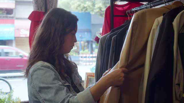 年轻女性成年人在旧货店浏览皮夹克视频下载