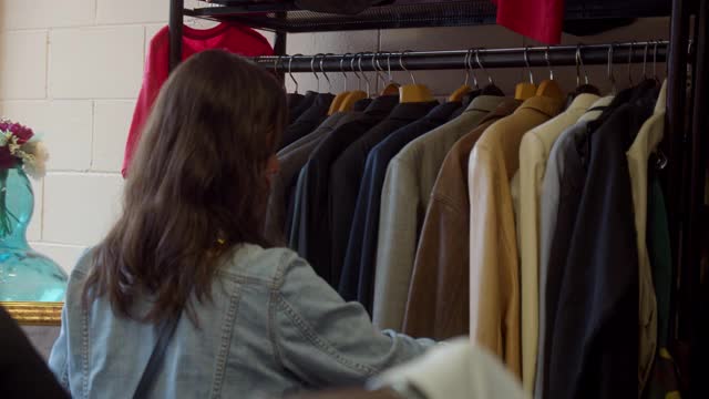 年轻女性成年人在旧货店浏览皮夹克视频下载