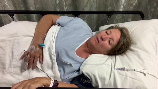 一个病人躺在病床上，带着静脉导管和脉搏血氧计视频下载