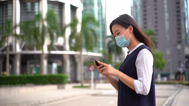 一名亚洲华裔女性戴着防护口罩，使用智能手机视频下载