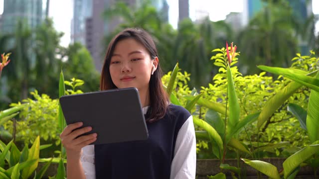 年轻的亚洲女商人在城市的一个户外公园使用数字平板电脑视频通话视频下载