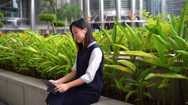 年轻的亚洲女商人在城市的一个户外公园使用数字平板电脑视频通话视频下载