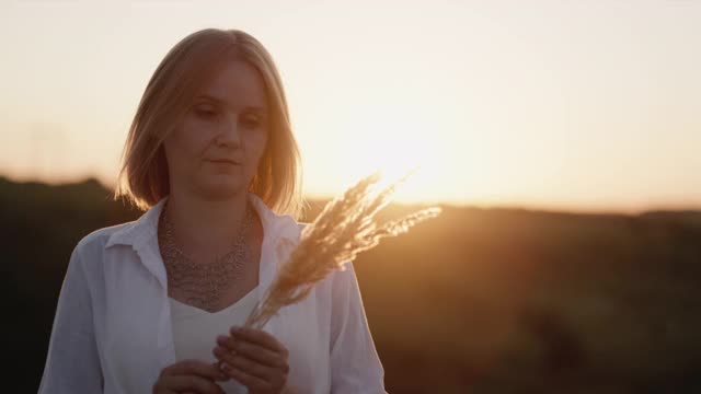 一个中年妇女的剪影在日落，拿着一片草视频下载