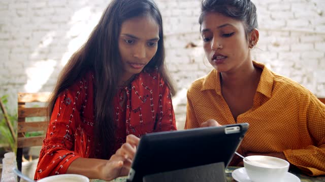 两个年轻的成年女性工作团队喝着茶咖啡，他们在笔记本电脑上视频下载