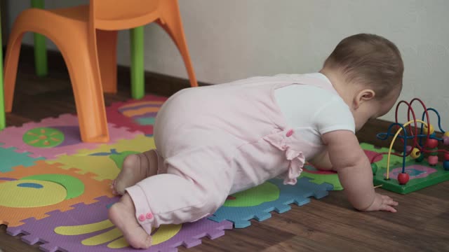 婴儿，童年概念-快乐有趣的蹒跚学步的孩子8个月的女婴坐在垫子上舔玩木制和钢丝珠迷宫算盘游戏。胖乎乎的醒着的新生儿在室内游戏室地板上爬视频下载