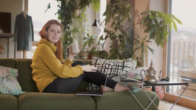 坐在沙发上用笔记本电脑打字的女人微笑着视频素材