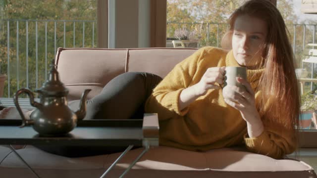 在阳光下坐在沙发上喝茶的女人视频素材