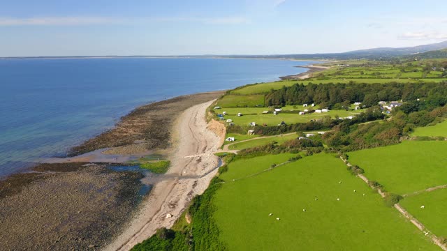 无人机拍摄田园诗般的绿色农田和田野在威尔士海岸在阳光明媚的夏天与低潮的海洋和海滩视频下载