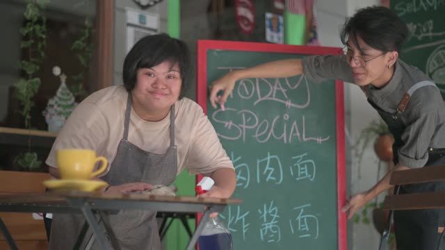 亚洲女性与唐氏综合症工作在一个咖啡馆清洁准备与她的同事打开业务视频素材