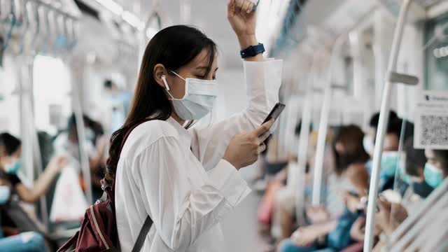 年轻的亚洲妇女戴着口罩在地铁使用电话视频素材
