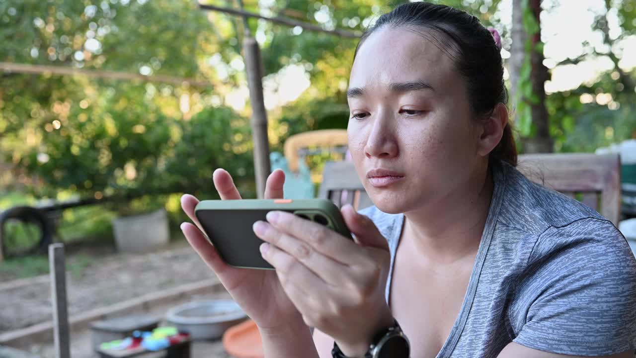社交媒体为女性使用智能手机的概念:亚洲女性坐着用手机阅读新闻似乎独自在家放松时间。视频下载