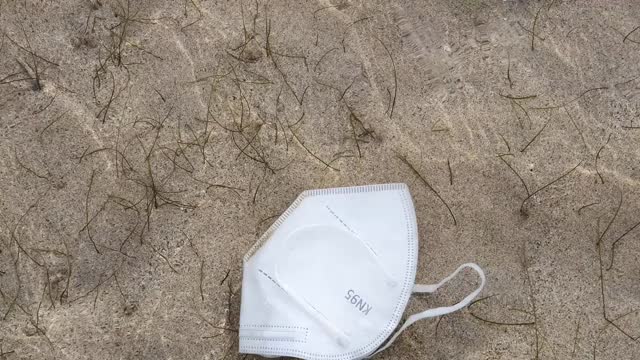 一种冠状病毒或COVID-19一次性口罩，被丢弃，现在作为塑料海洋垃圾漂浮在海岸线附近的海上视频素材
