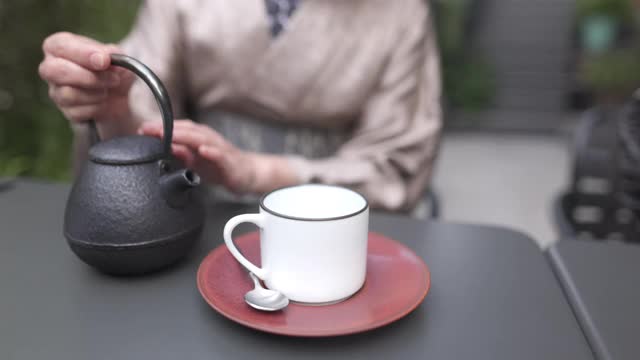 穿着和服的日本妇女在户外咖啡馆向茶杯倒热茶视频下载