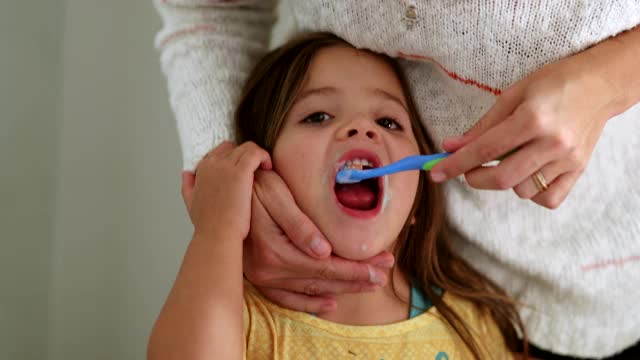 父母在女儿睡觉前刷牙。妈妈用牙刷给小女孩刷牙视频素材