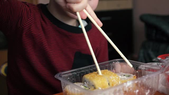 一个有食欲的高加索学龄前男孩用筷子吃日本寿司。孩子用筷子吃饭。选择性聚焦，浅景深视频素材