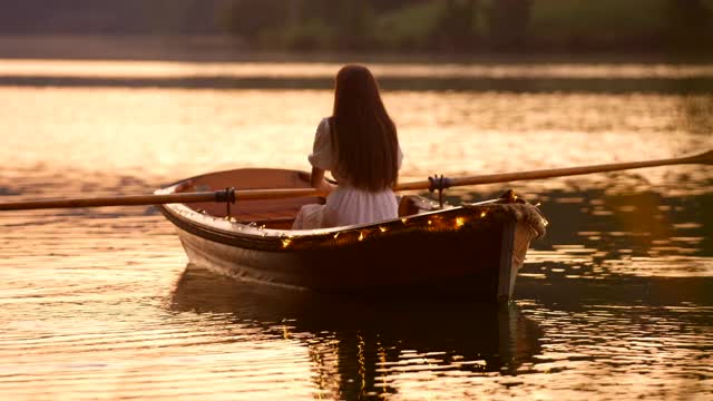 日落时分，年轻女子在装饰华丽的小船上划水视频素材