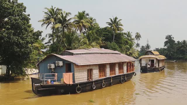 印度喀拉拉邦回水区，漂浮在流经棕榈树的河流上的船屋视频下载