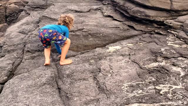 蹒跚学步的孩子爬上岩石巨石的大自然视频下载