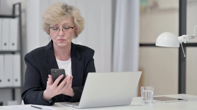 老女商人一边使用智能手机一边使用笔记本电脑视频素材