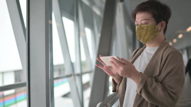 一名戴着防护口罩的亚洲华人女性在城市桥梁上行走，用智能手机app查看金融股市场分析，受新冠肺炎疫情影响呈下降趋势。忙碌的生意视频素材