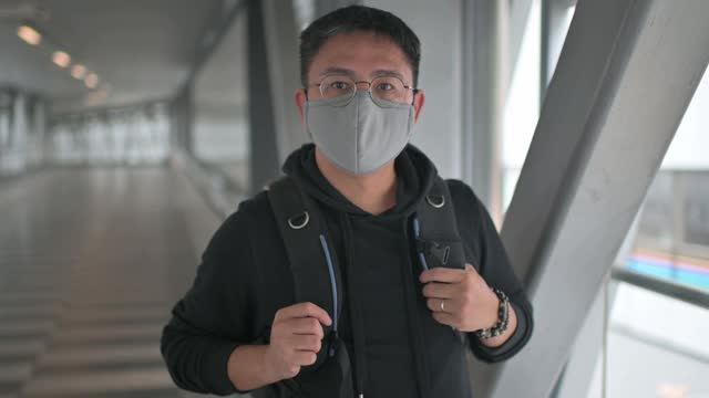 一名亚洲华人戴着防护口罩走在城市的桥上，在市中心通勤上班视频素材