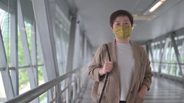亚洲华人妇女戴着防护口罩走在城市的桥上，在市中心上班视频素材