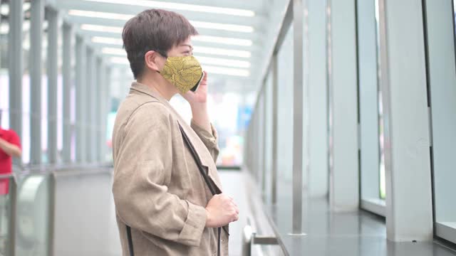 亚洲华人妇女戴着保护面罩，在城市中通过电话进行商业活动视频素材