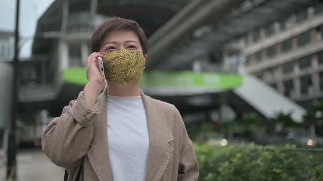 亚洲华人妇女戴着保护面罩，在城市中通过电话进行商业活动视频素材