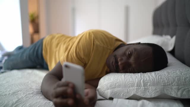 疲惫的老人躺在家里的床上使用智能手机视频素材