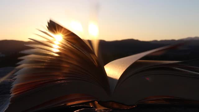 灵感与智慧理念。打开书随书页在风中移动在夕阳或日出的阳光，温暖的光。视频素材