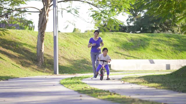 亚洲母亲慢跑和她的儿子骑平衡自行车。视频素材