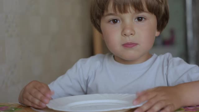 孩子吃披萨。饥饿的小男孩坐在家里厨房的桌子上吃着美味的意大利披萨。不健康的营养快餐。一个吃午饭的孩子的肖像。面对小男孩特写。视频素材