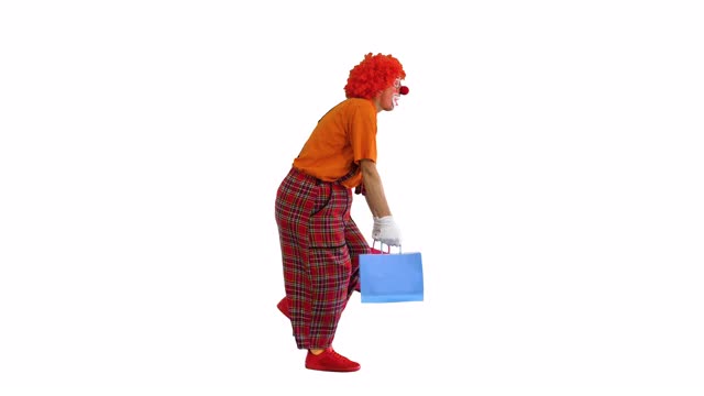滑稽的小丑拿着沉重的购物袋走在白色的背景上视频素材