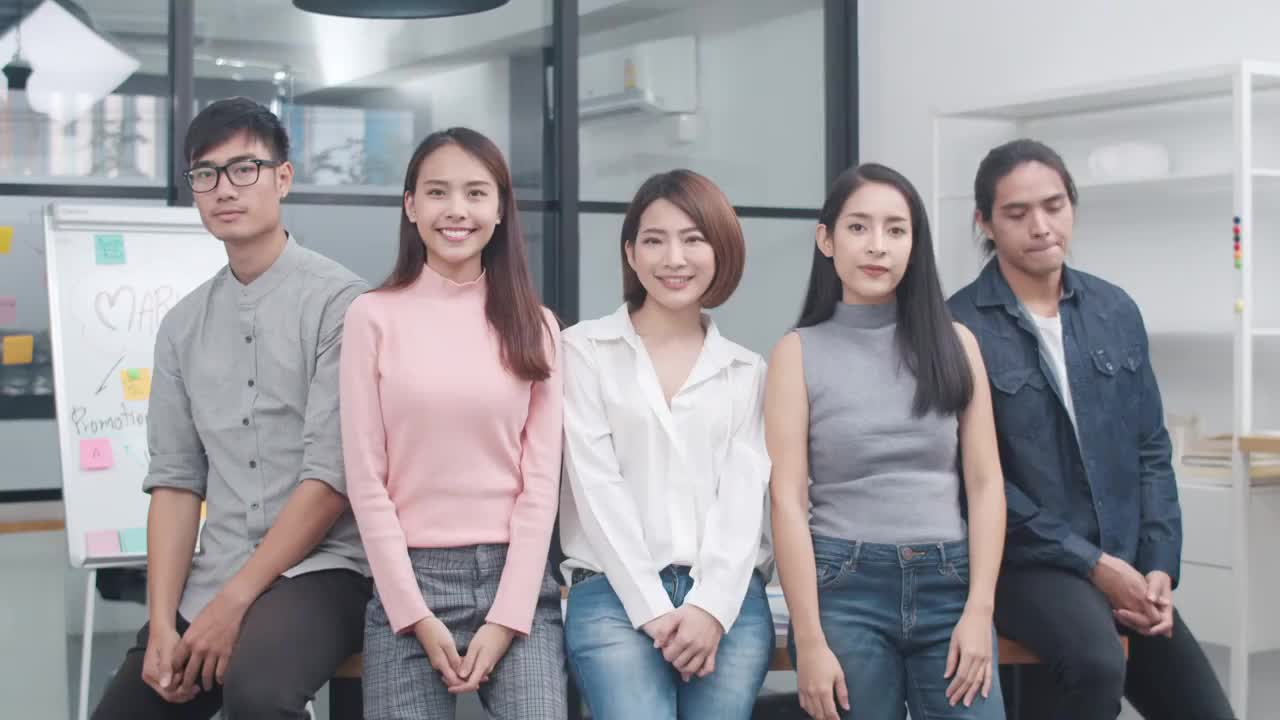 亚洲青年创意人士在时尚休闲穿着微笑和双臂交叉在创意办公室的工作场所。不同的亚洲男性和女性站在一起创业。视频素材