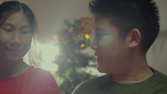 可爱的亚洲兄妹在家里亲吻拥抱，以圣诞装饰为背景，慢镜头。视频下载