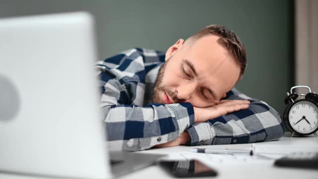 劳累过度的男经理在辛苦工作一天后睡在办公桌上。近距离拍摄4k红色相机视频素材