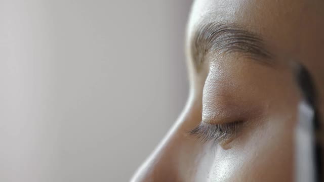 化妆师正在刷眉毛，以塑造女性化妆的侧视图视频素材