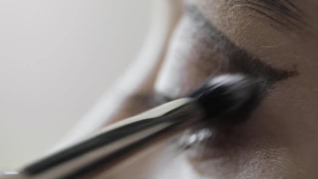 化妆师在年轻女子上眼睑涂抹眼影，眼部特写视频素材