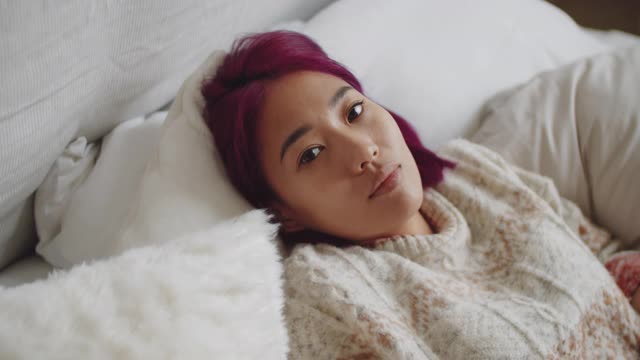 年轻的亚洲女子躺在床上，为相机摆姿势视频下载