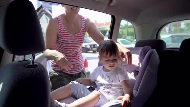 妈妈把可爱的小女孩放在汽车后座的安全座椅上视频素材