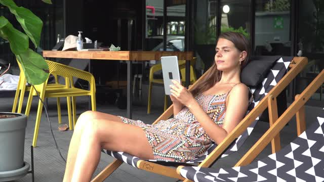 一个白人年轻女子在一个豪华酒店度假，有休闲活动与心情愉快和享受使用数字与软饮料从男服务员来提供软饮度假期间，躺在沙滩椅上。视频下载