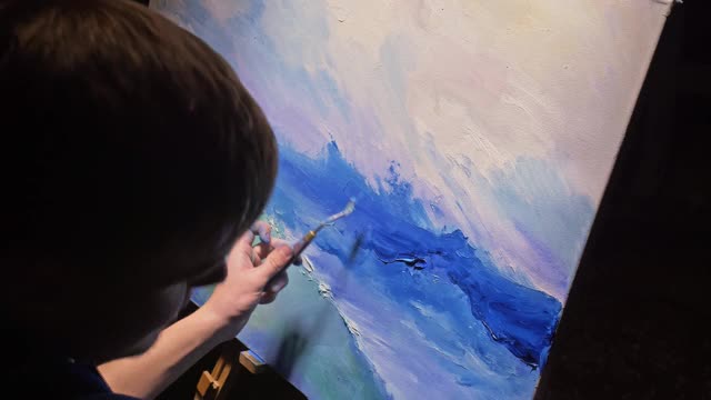 临摹画家用海洋中的船画海景。工匠装饰师用丙烯酸油的颜色绘制了蓝色海面上的船帆。画刷子，刀调色板。视频下载