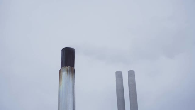 锅炉房白色的金属管在阴天的映衬下冒着烟。烟从烟囱逸出，消散到空气中。视频素材