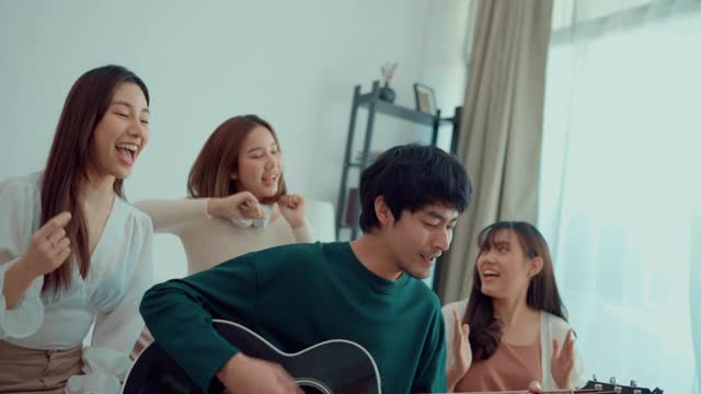 年轻的亚洲男子弹着吉他，周围是一群年轻女子，他们在室内开“轰趴”视频素材