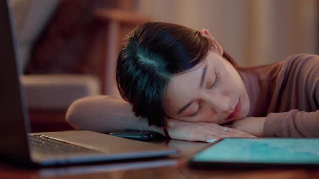 困倦而疲惫的亚洲女性在深夜坐在家里的办公桌前，用笔记本电脑和数字平板电脑阅读课程。视频下载