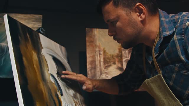 一个穿蓝衬衫的艺术家在画布上画画。视频素材