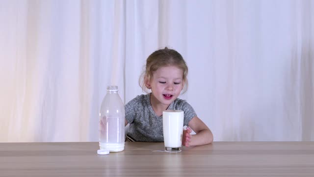 女孩和牛奶。倒进瓶子里，从玻璃杯里喝水。开朗的孩子。视频下载